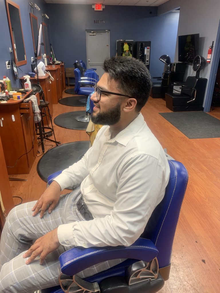 A man wearing glasses in a white shirt facing towards a mirror looking at his new haircut.