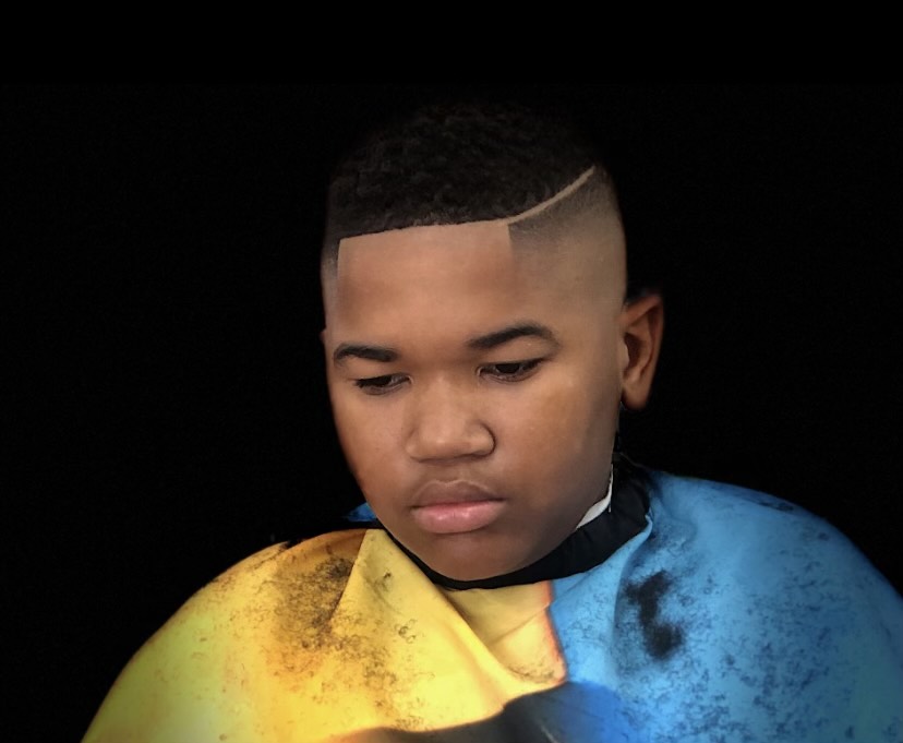 Young boy in a yellow and blue barber cape, looking down after his haircut.