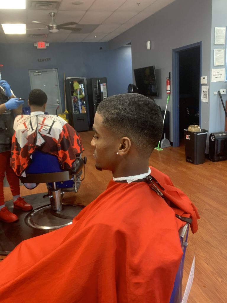 A picture of a young man in a red barber cape sitting on a barber chair after his haircut.