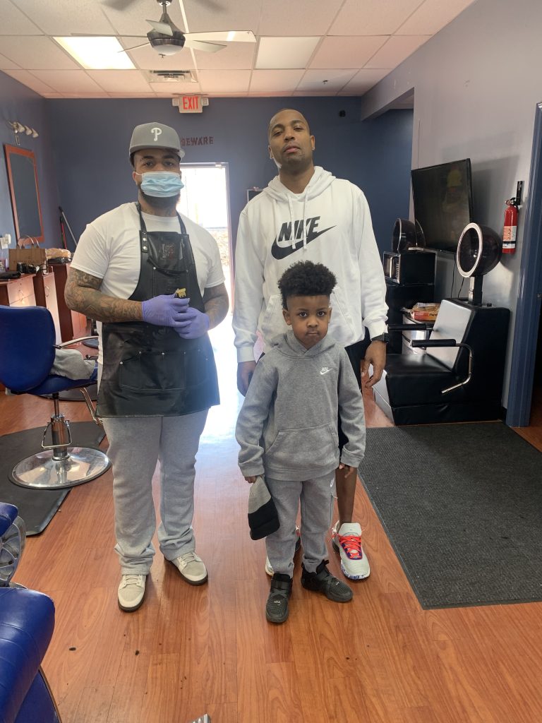 A barber standing next to a young child and his father after a haircut.