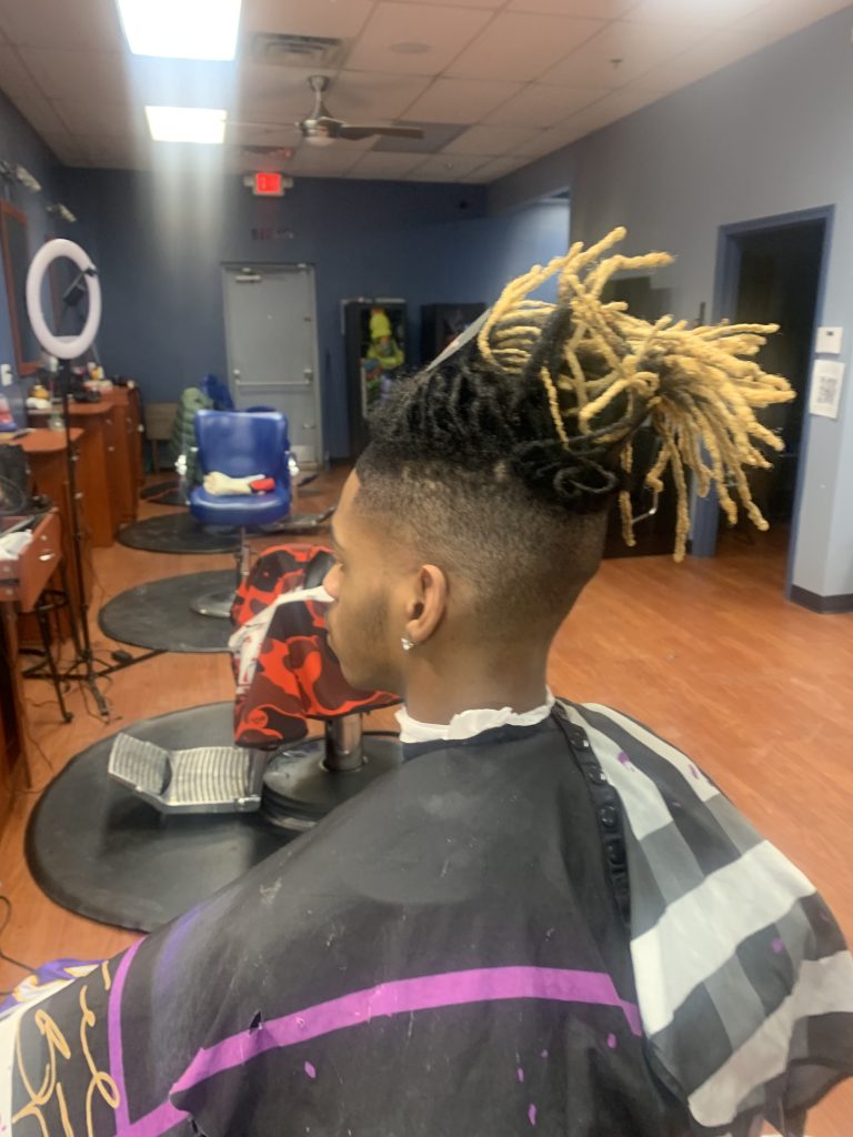 A young man with twist hairstyle with blonde tips sitting in a barber chair.