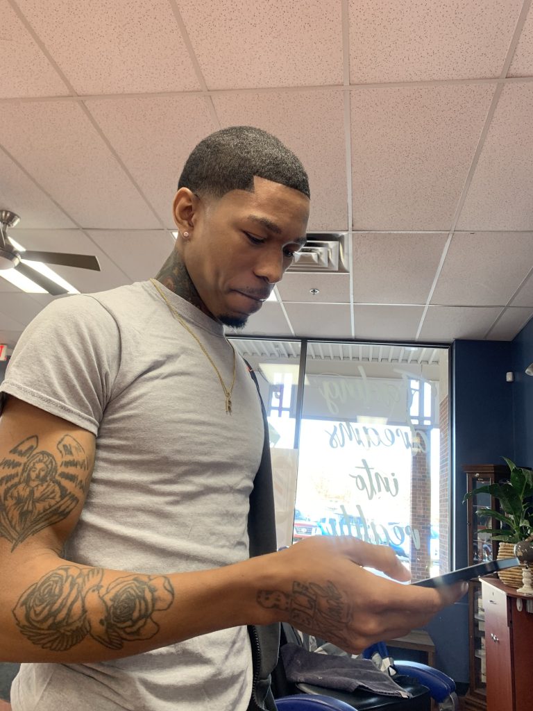 Young man standing looking at his cellphone after a haircut.