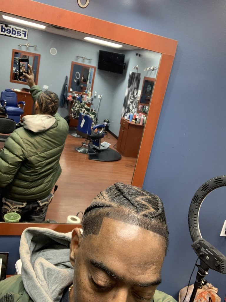 Gentleman taking a selfie against the barbershop mirror of his hair braids.